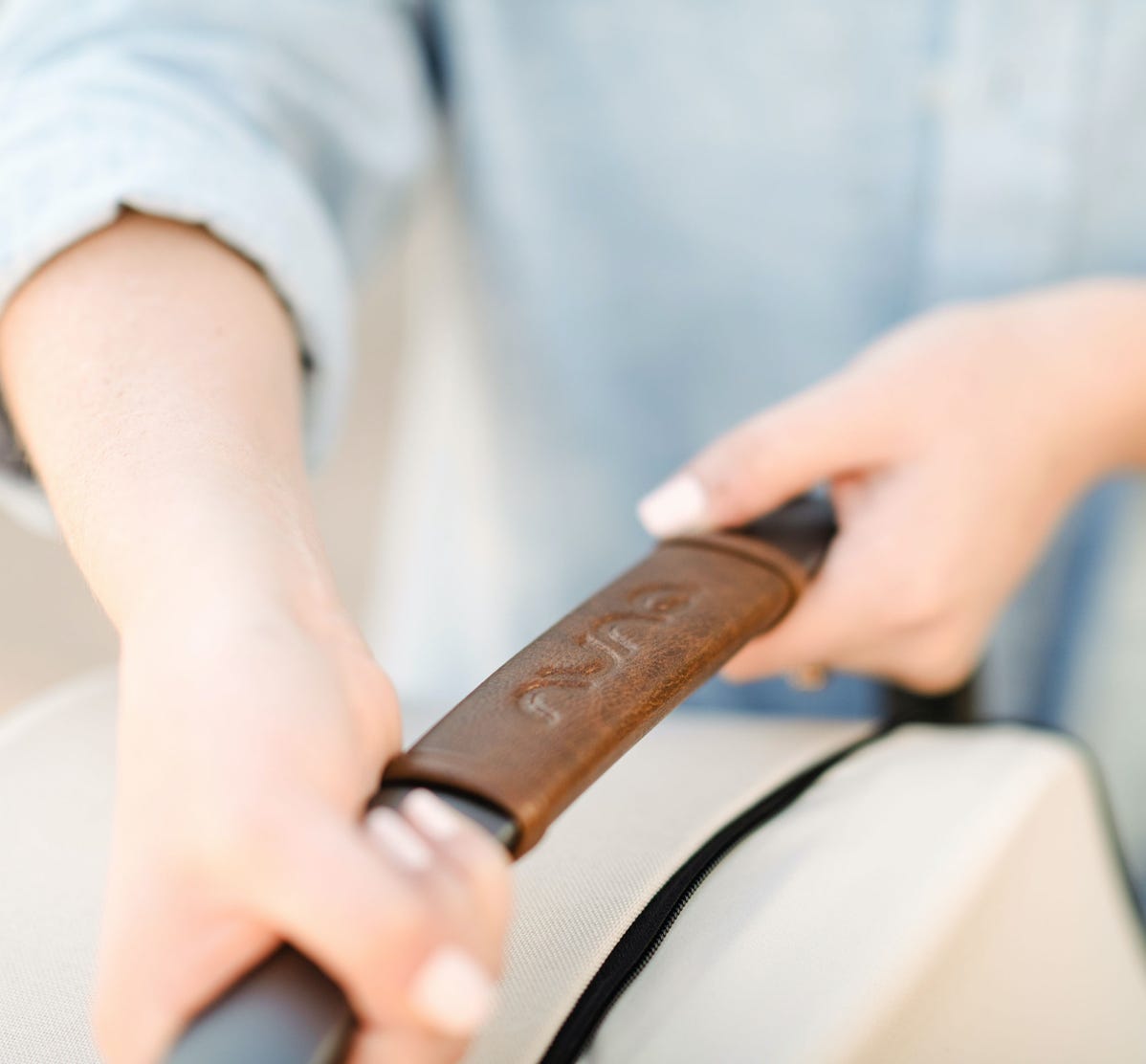 Women's hands holding leatherette handle of a Nuna infant car seat