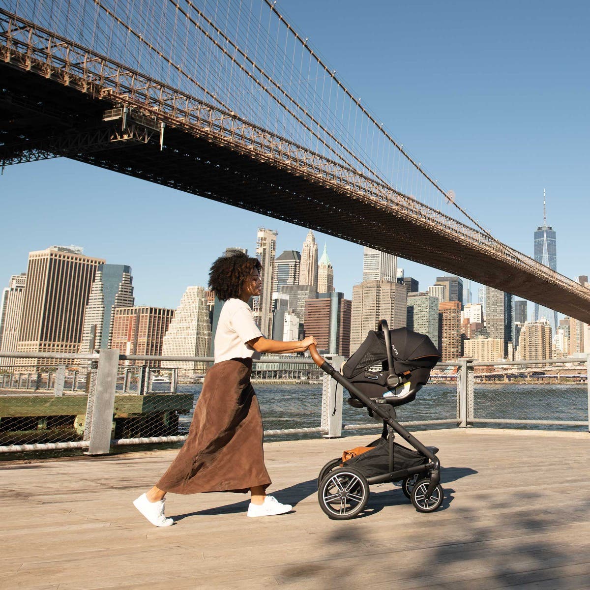 Woman pushes PIPA urbn car seat on MIXX next stroller frame in front of cityscape 