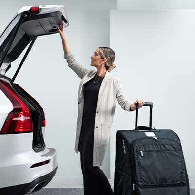 Woman opens vehicle trunk with Nuna wheeled travel bag 