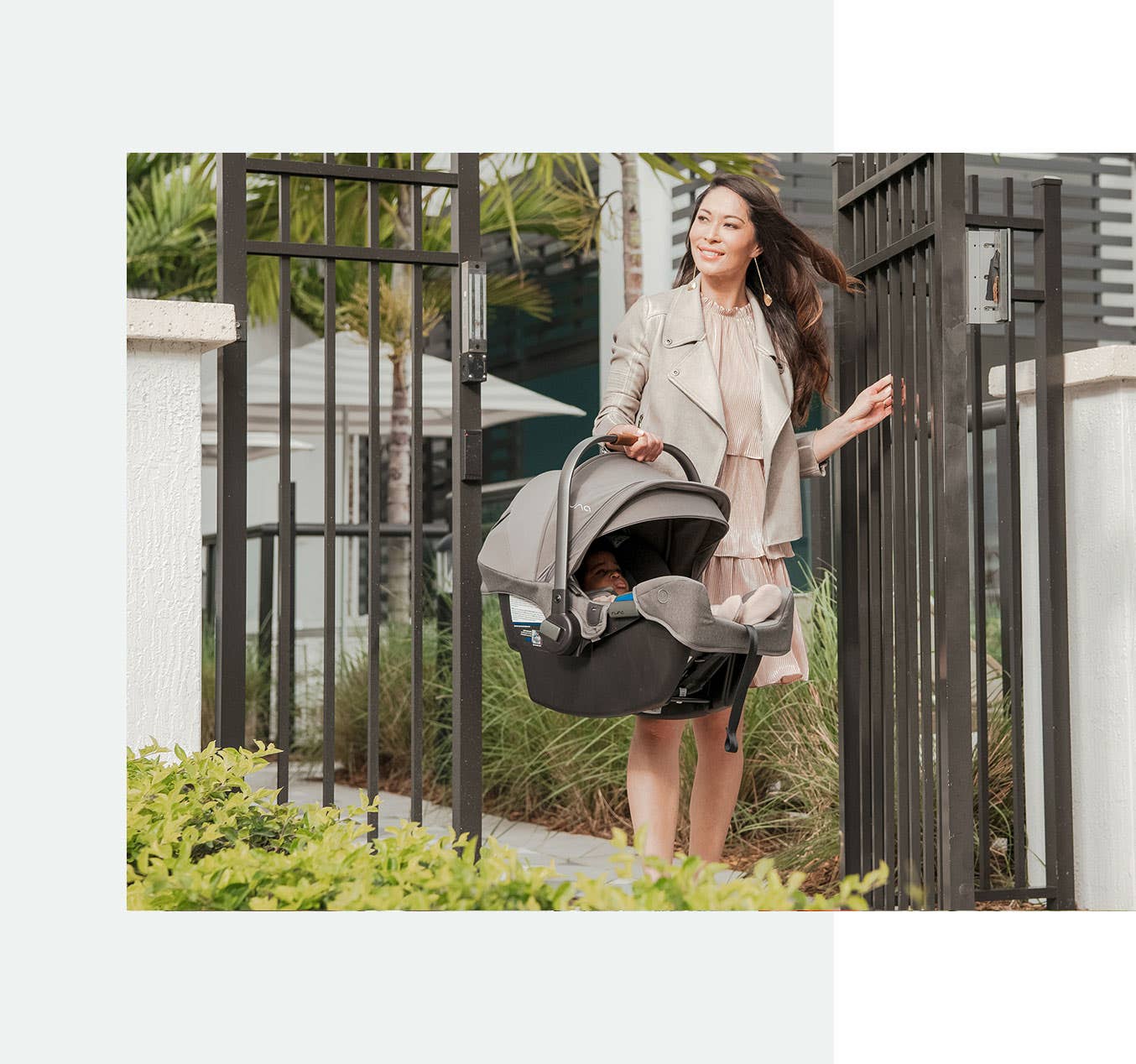 Woman in dress walking through iron gates carrying lightweight Nuna infant car seat